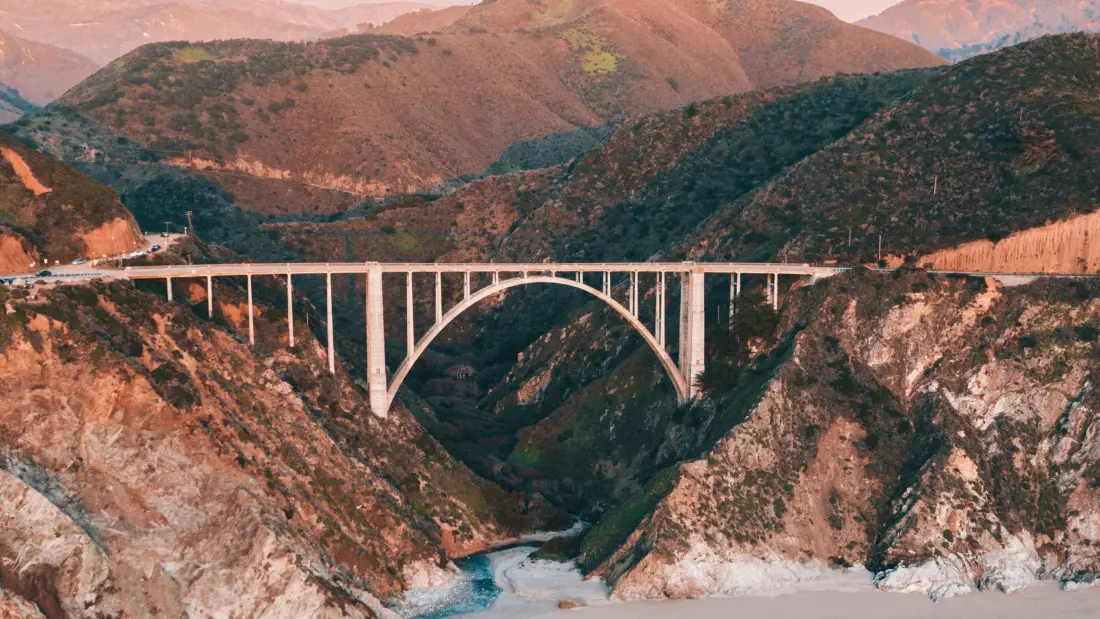 Pont en arc reliant deux falaises, métaphore de l'UX comme langage commun pour unifier la vision produit et réaliser l'alignement business tech
